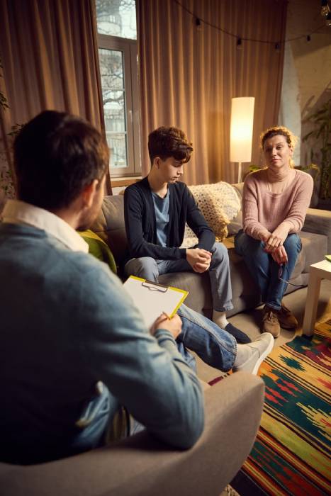 Man, psychologist discusses strategies with a teenage boy and his mother during a therapy session, emphasizing emotional support and understanding. Concept of psychology, assistance, therapy